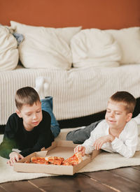 Two boys lie on the floor eating pepperoni pizza from a box. vertical frame. 