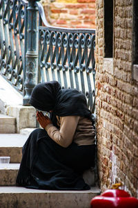 Rear view of man sitting against wall