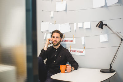 Creative businessman talking on mobile phone while sitting at desk in office