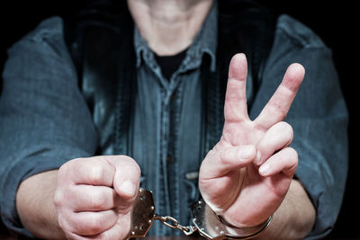 Midsection of criminal showing peace sign while sitting in prison