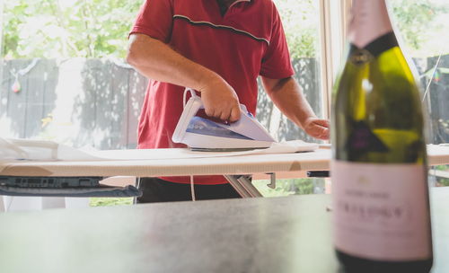 Champagne bottle on table against man ironing cloth at home