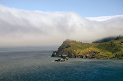 Scenic view of sea by mountain against sky