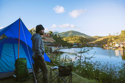 Side view of man standing by lake against sky