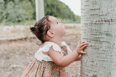 Side view of girl standing by tree