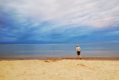 Rear view of man standing on beach against sky