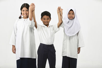 Portrait of friends wearing school uniform holding hands against white background