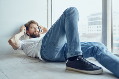 Young man listening music while lying down on floor by window