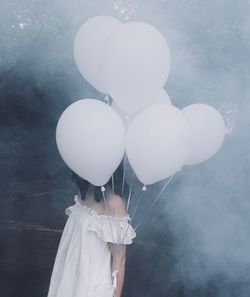 Woman covering face by balloons amidst smoke