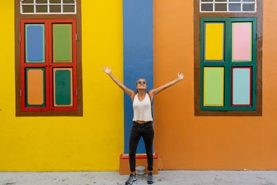 Full length portrait of woman standing against yellow wall