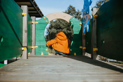 Rear view of girl sitting on wooden floor outdoors