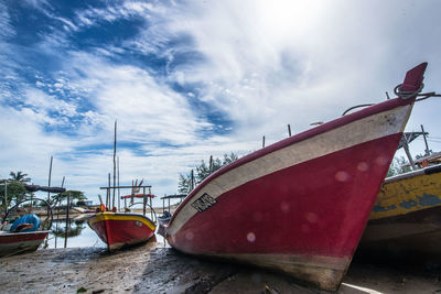 Boats moored on lakeshore against cloudy sky