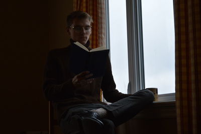 Man looking away while sitting on window at home