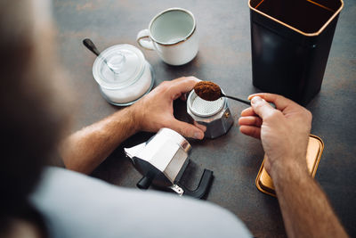 Unrecognizable man filling an italian coffee maker at the kitchen bar