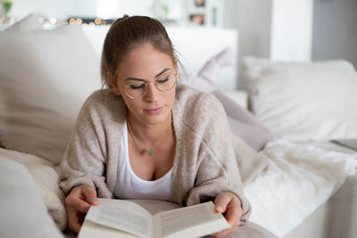 Young woman reading book while lying on bed at home