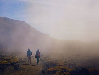 Rear view of men walking on road against mountain and sky