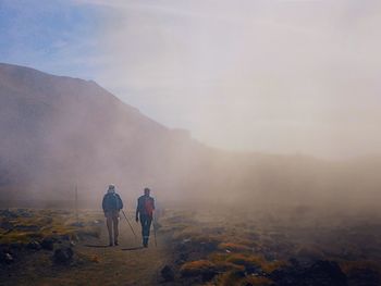 Rear view of men walking on mountain against sky