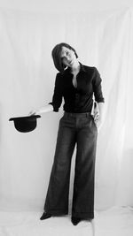 Young woman holding hat while standing against white background