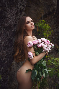 Naked woman holding bouquet while standing against tree