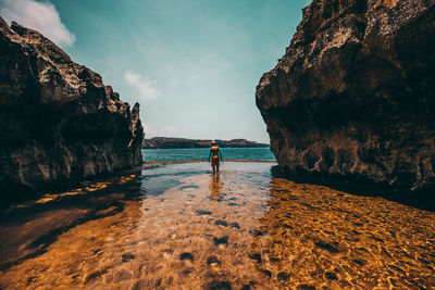 Man standing on rock by sea against sky