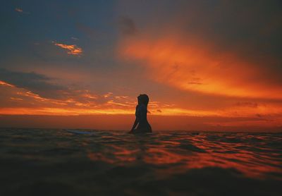 Silhouette young woman surfing on sea against cloudy sky during sunset