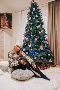 Beautiful young girl sitting next to the christmas tree. new year decoration. home interior. winter 