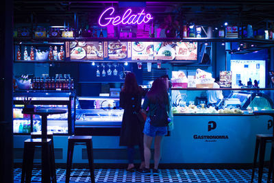 Rear view of people standing at illuminated shop