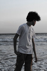 Rear view of man standing at beach against sky