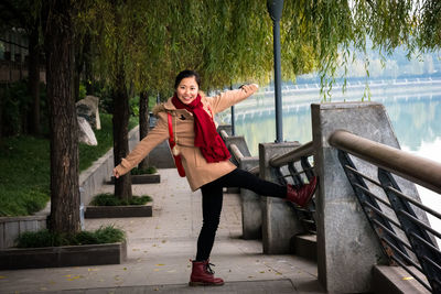 Portrait of smiling young woman posing on footpath by lake