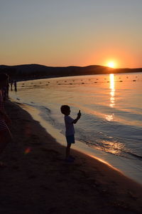 Rear view of silhouette man standing at beach during sunset