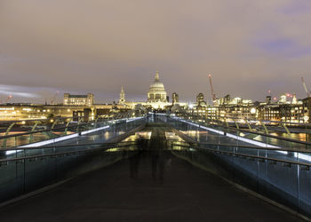 Double exposure of people on bridge against illuminated cityscape