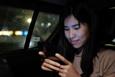 Asian woman sitting in a car using mobile phone, video calling, online app.