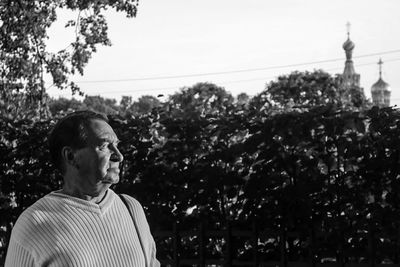 Thoughtful man standing by plants against clear sky