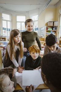 Boys and girls looking at teacher helping them in classroom