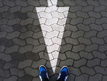 Low section of person standing arrow sign on footpath