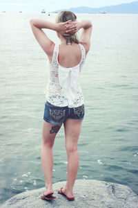 Rear view of woman standing on rock at beach