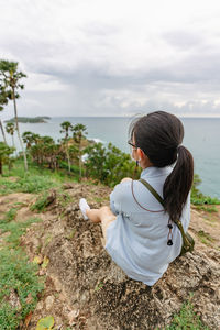 Rear view of woman standing on rock against sky