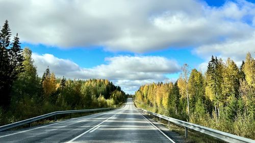 Empty road along trees and against sky