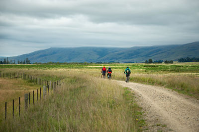 Group of people on field by road against sky