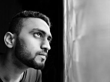 Close-up of young man looking through window at home