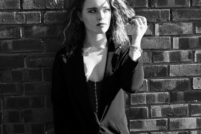 Young woman standing against brick wall black and white 