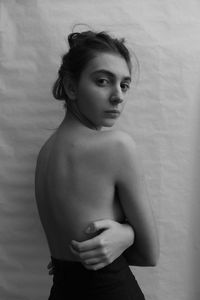 Portrait of shirtless woman standing against wall