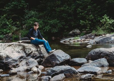 Young woman sitting on rock against trees