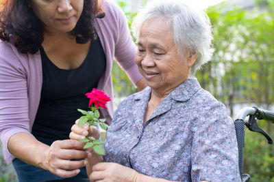 Asian elderly woman holding red rose flower, smile and happy in the sunny garden.