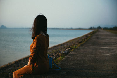 Rear view of woman sitting by sea against sky