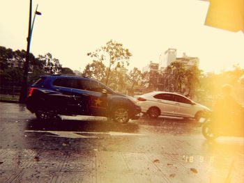 Cars on wet street against sky in city