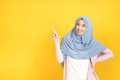 Young woman standing against yellow background