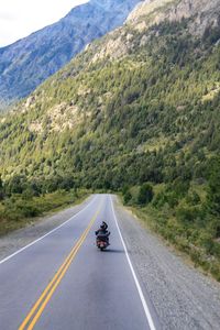 Rear view of man riding motorcycle on road leading towards mountains