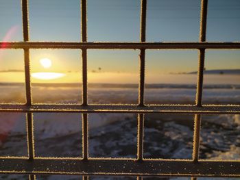 Close-up of metal fence against sky during sunset