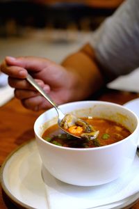 Midsection of person holding soup in bowl on table