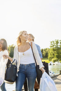 Happy friends with luggage walking on pier against clear sky